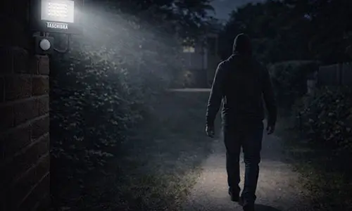 Homem caminhando no quintal escuro, acionando o sensor e iluminando durante apenas em sua presença garantindo economia na conta de luz.